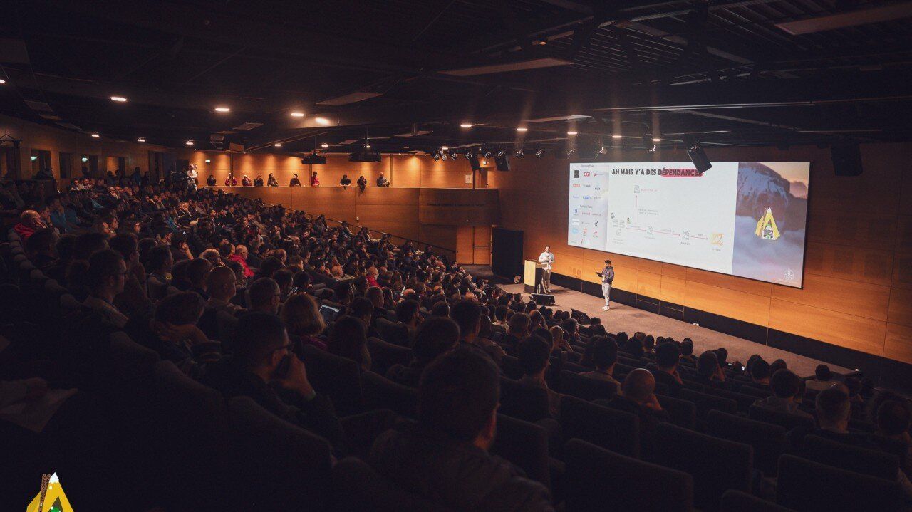 Amphithéâtre comble de SnowCamp face à deux orateurs sur scène et leurs slides